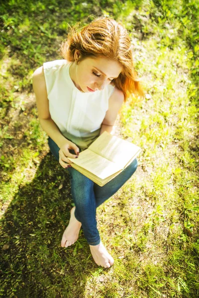 Üstten Görünüm. Taze yeşil çimenlerin üzerinde otururken kitap okuma kız.