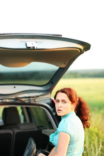 Молодая Рыжая Женщина Открывает Багажник Своей Машины Фоне Зеленого Поля — стоковое фото
