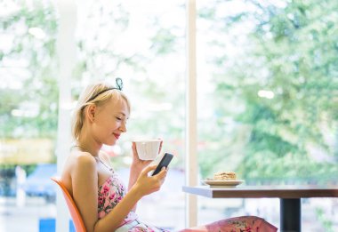 sarışın kadın telefonu kafede kullanarak. Parlak güneşli sabah kafede. 