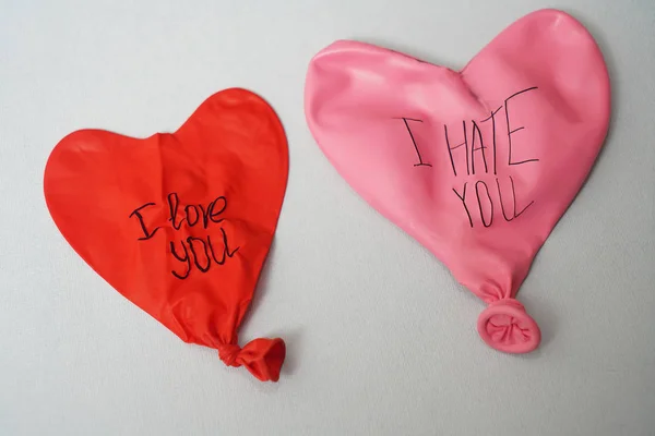 couple of deflated  balloons with the words: i hate you and i love you on paper texture background. two rubber  balloons