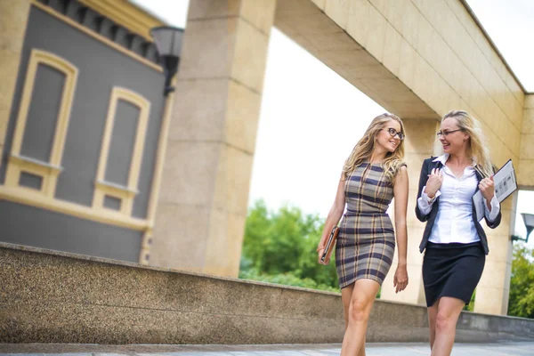 Full length of happy young businesswomen with mobile phone and suitcase walking on street