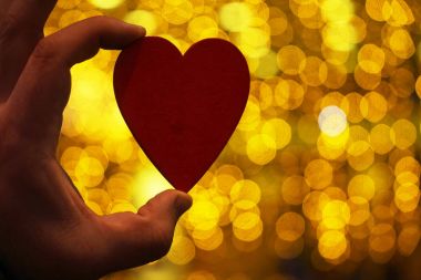 male hand holding  wooden heart against yelllow golden bokeh background. Happy Valentines day. 14 february clipart