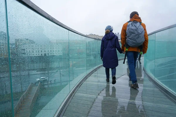 photo of two young people walking  in city in rain. Water drops on glass. Concept of seasons, modern city.