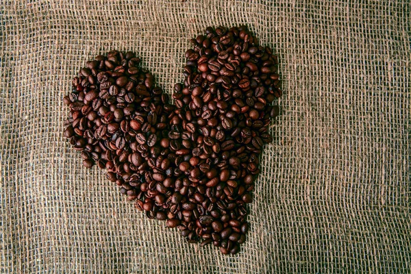 Coffee beans in the shape of a heart on the background of sacking. Heart coffee frame made of coffee beans on burlap texture