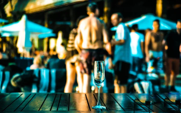 glass  against group of dancing people. Hot beach party. Sexy people. focus on empty transparent glass