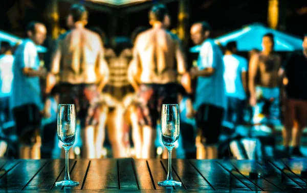 glasses  against group of dancing people. Hot beach party. Sexy people. focus on empty transparent glasses