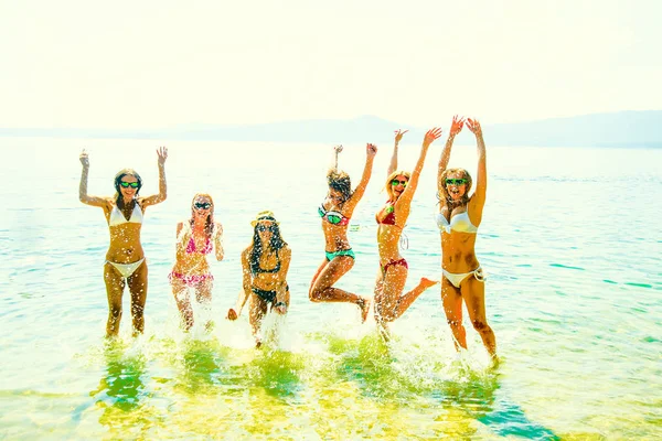 young group of women  jumping in ocean at sunset. Team of adult girls jumping  in water