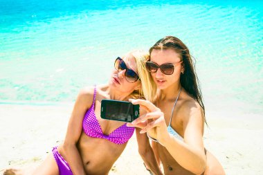 iki genç kadın plajda selfie smartphone ile yapım gülümseyen su doku arka plan mavi