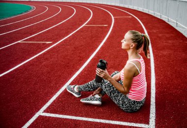 Çömelp yolda ve içme suyu plastik shaker dan oturan sarışın kadın.