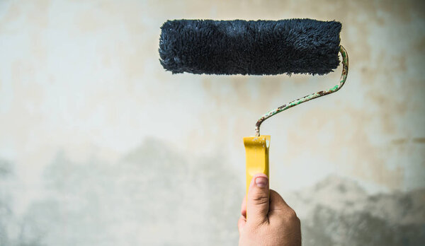 man painting in concrete wall with dry brush. male Hand holding rolling paint brush