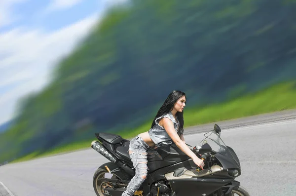 黒のスポーツ バイクに座って美しいブルネットの女性の肖像画 デニムのベストを身に着けている非常に熱いセクシーな若い女の子 — ストック写真