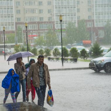 Kazakistan, Astana-06 Temmuz 2016: üzgün aile yağmurlu sokakta yağmur altında yürümek. Aile kızı çalıştıran şemsiyesi altında. Yağmurlu bir gün.