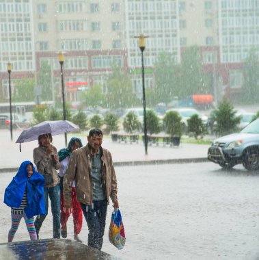 Kazakistan, Astana-06 Temmuz 2016: üzgün aile yağmurlu sokakta yağmur altında yürümek. Aile kızı çalıştıran şemsiyesi altında. Yağmurlu bir gün.