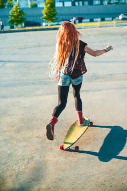 Kaykay üzerinde geri dikiz kadın. Kızıl saçlı Genç kadının kaykay tam uzunlukta  