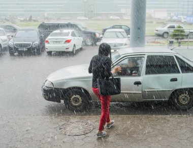 Kazakistan Astana - 06 Temmuz 2016. Arabalar arasında yağmur altında ıslak yaya Asyalı. 