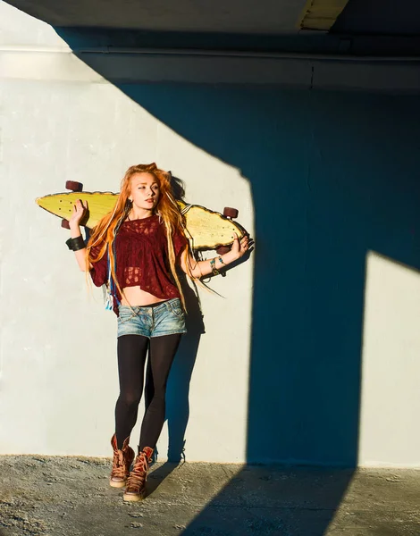 portrait of teen girl with long skate board standing  against gray wall.