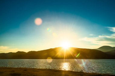 Dağlar üzerinde güzel puslu gündoğumu. Deniz kıyısında sun ray yansıması dalgalı su yüzeyi ile 