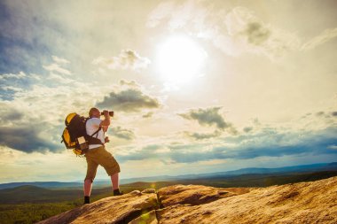 Turist ve fotoğrafçı dağ üstten güneşli bulutlu gökyüzü üzerinde dürbün ile bizi izliyor. 