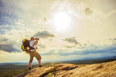 Turist ve fotoğrafçı dağ üstten güneşli bulutlu gökyüzü üzerinde dürbün ile bizi izliyor. 
