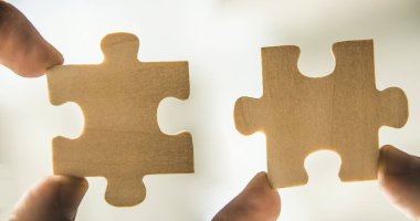 Kahverengi ahşap bulmacanın parçaları tutan parmak. Beyaz arka plan üzerinde izole. 