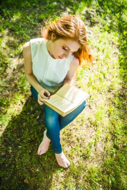 Üstten Görünüm. Taze yeşil çimenlerin üzerinde kitap okuma kız. Bahar zaman sezon.