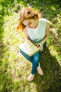 Üstten Görünüm. Taze yeşil çimenlerin üzerinde kitap okuma kız. Bahar zaman sezon.