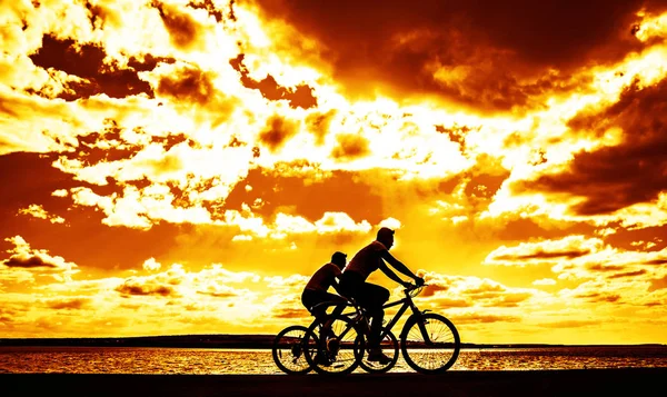 运动的朋友在自行车在日落 骑自行车的人沿着海岸 体育在自然背景 — 图库照片
