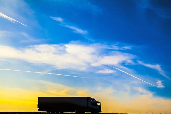 Silhouette of a moving truck at sunset. Truck on asphalt highway in a rural landscape at sunset.