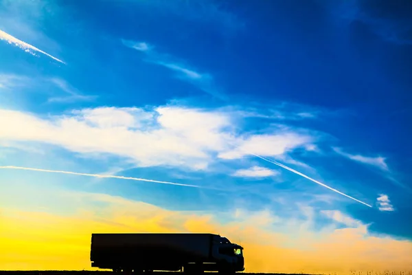 日落时移动卡车的剪影 日落时农村景观中的沥青公路卡车 — 图库照片