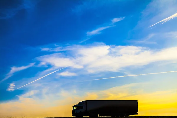 Silhouette of a moving truck at sunset. Truck on asphalt highway in a rural landscape at sunset.