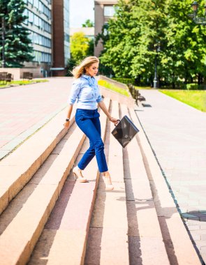 Genç ve güzel bir iş kadını evrak çantasıyla merdivenlerden iniyor. 