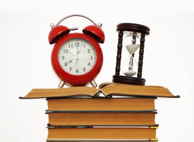 Beyaz arka plan üzerinde izole kitap yığını üzerinde kum saati ile kırmızı vintage çalar saat.