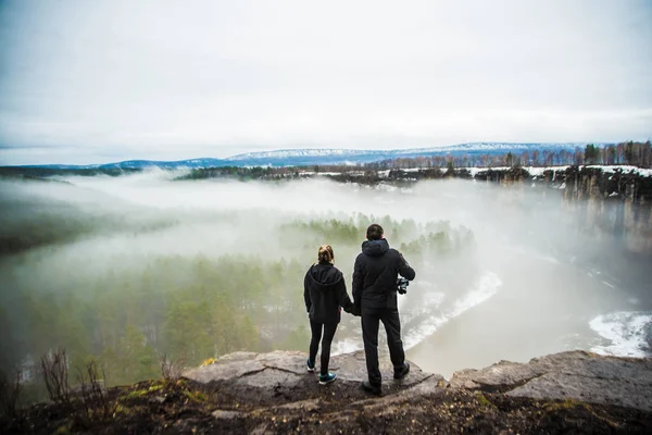 back rear view of male and Female travelers facing the mountains covered in fog