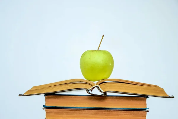 Open book on a pile of books and green apple isolated on white background. healthy food and education. back to school idea