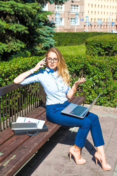 Şehir arka plan üzerinde parkta bankta oturmuş ve dizüstü bilgisayarda çalışan bir iş kadını. İş kadını 