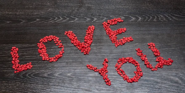 Close up of festive decoration for Valentines day on black wooden background.  words Love you  from many red  confetti