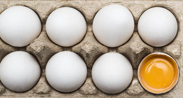 eggs in egg tray, one egg cracked. Group of white fresh eggs