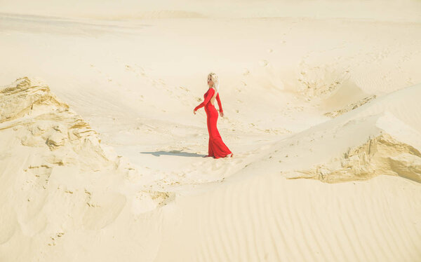 Girl in long red dress  walking on sand dunes.