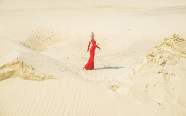 Girl in long red dress  walking on sand dunes.