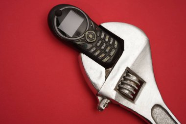 İngiliz anahtarı ve bir kırık cep telefonu kırmızı kağıt arka plan üzerinde yaşları