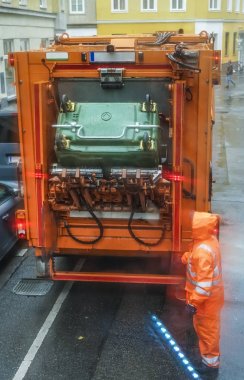 Görünümü top turuncu çöp kamyonu ve su geçirmez üniforma, işçi. Avrupa sokak