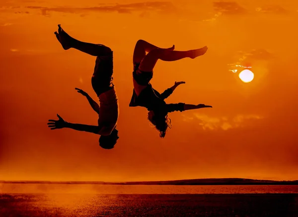 ビーチで家族 カップル 夕日を背景にビーチでジャンプ男女のシルエット — ストック写真
