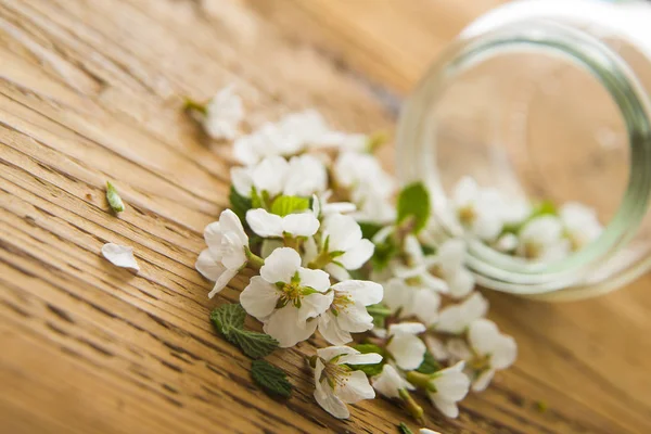 bouquet of white spring flowers and  transparent jar on wooden table background.