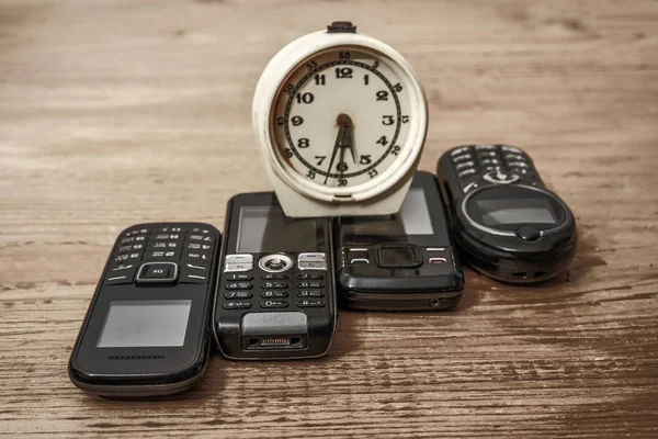 alarm clock and vintage   mobile phones. wooden table background.