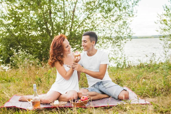 快乐的年轻夫妇在野餐 男人用蛋糕喂女人 — 图库照片