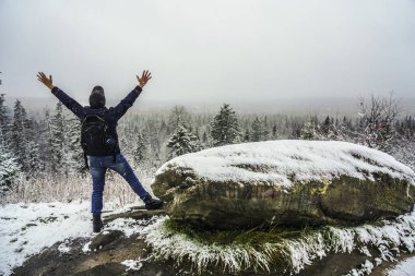 Sırt çantalı, sırt çantalı, sırt çantalı turistin arkadan görünüşü alacalı orman dağlarında karla kaplı ve bulutlu gökyüzü arka planında kollarını kaldırmış. Eller yukarı.. 