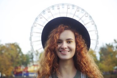 Dönme dolapta kameraya bakan zarif bir kadın lunaparkta yuvarlak şapkalı ve sonbahar elbisesi giymiş..