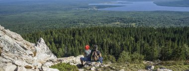 Orta yaşlı çiftin uçurumun kenarındaki dağlarda oturup manzaranın tadını çıkarırken çekilmiş bir fotoğrafı. geri.