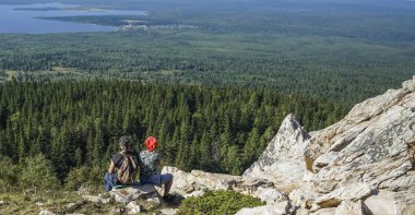 Orta yaşlı çiftin uçurumun kenarındaki dağlarda oturup manzaranın tadını çıkarırken çekilmiş bir fotoğrafı. geri.