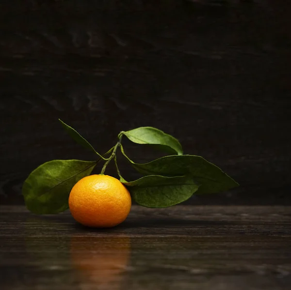 Fresh, ripe tangerine  with leaves on a black stone surface. Orange and green. Seasonal citrus fruit